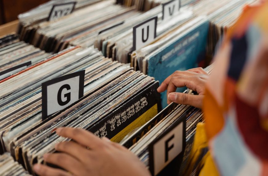 Hands flipping through alphabetically organized vinyl records, labeled dividers showing letters G and F, browsing in a record store