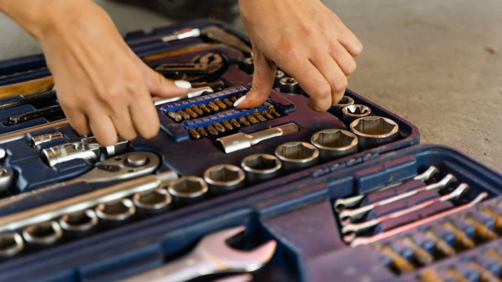Person organizing metal wrenches and sockets in a blue tool case, hands selecting tools, various tools neatly arranged, working on a flat surface indoors