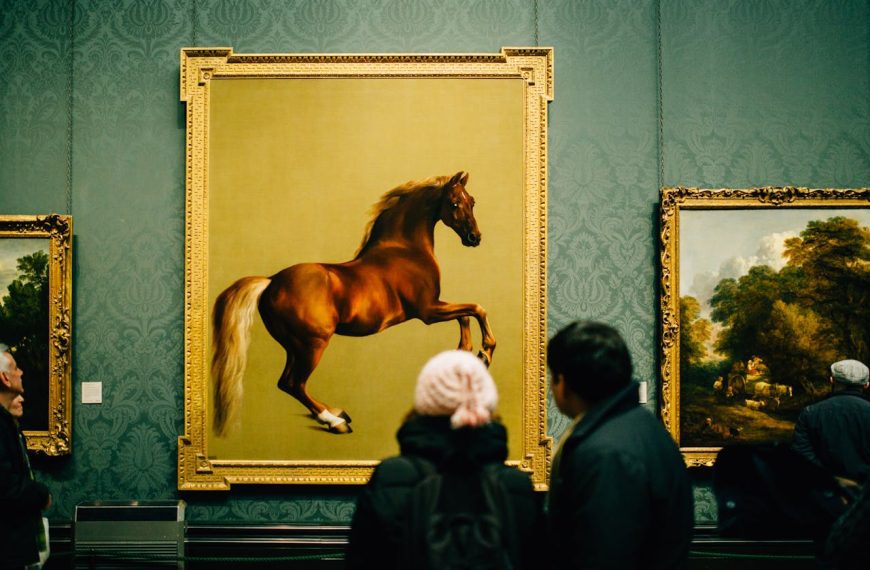 Two people viewing a large painting of a leaping brown horse in a gold frame, displayed on a green wall in an art gallery, surrounded by other framed artworks