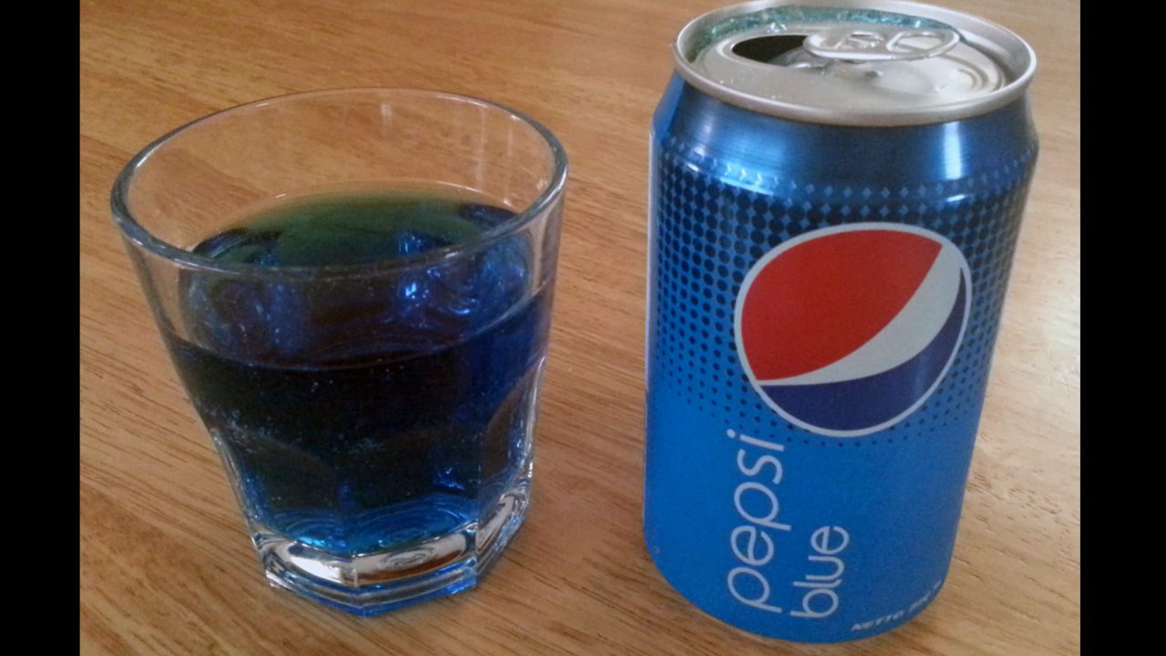 Can of Pepsi Blue next to a glass filled with bright blue soda, both placed on a wooden surface