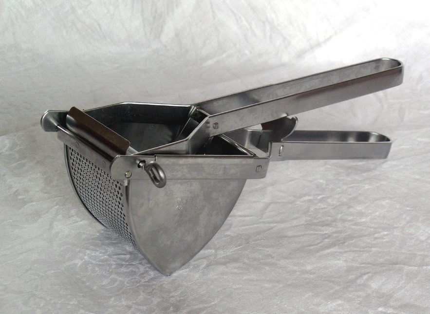 Metal potato ricer, two long perforated handles, hinged pressing mechanism, round perforated chamber, resting on a white textured surface