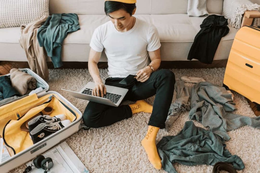 man enjoying screen time, ignoring messy house, cluttered room, focused on laptop, dishes stacked, laundry piled, relaxed posture