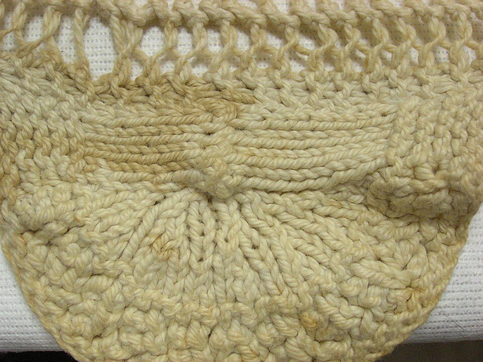 Close-up of a beige crocheted doily, intricate thread pattern, circular design, textured fabric, handmade lace decoration