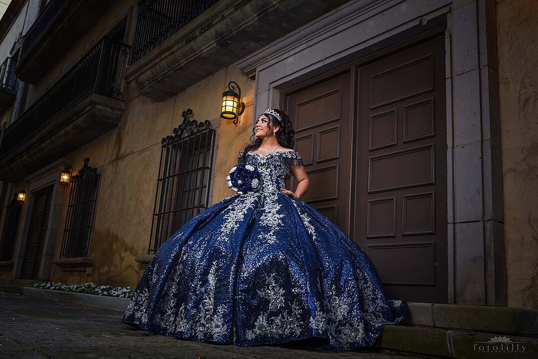 Woman in a royal blue ball gown, silver floral embroidery, standing outside a historic building, dressed for a formal event or themed photoshoot, elegant and regal appearance