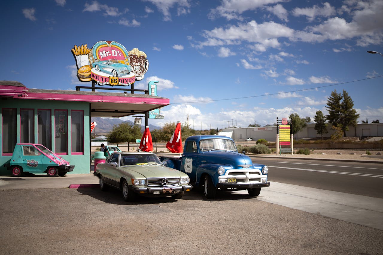Vintage cars parked outside Mr. D'z Route 66 Diner under a bright blue sky with scattered clouds and desert scenery