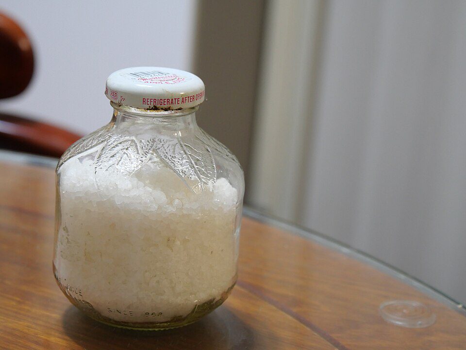 Glass jar filled with white substance, sealed with a white lid, placed on a polished wooden table