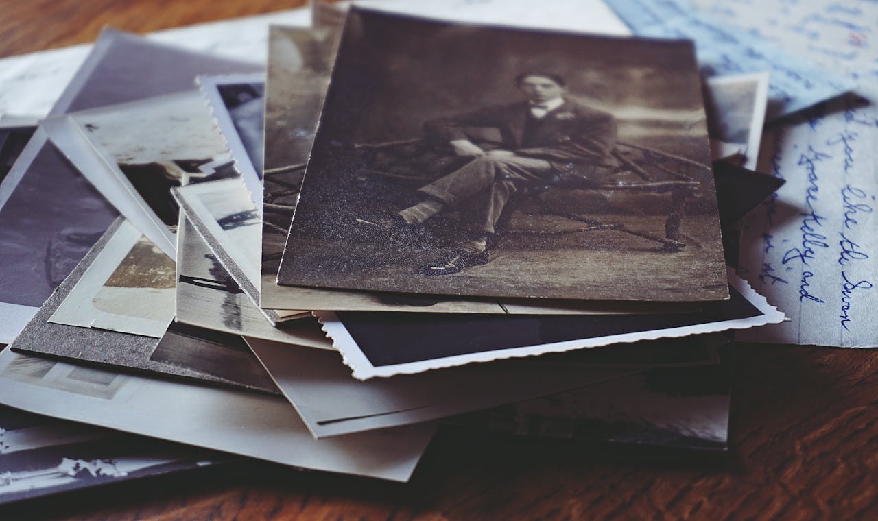 Scattered vintage photographs, black and white and sepia tones, nostalgic family memories, old paper textures, wooden surface background, aged and worn photo edges