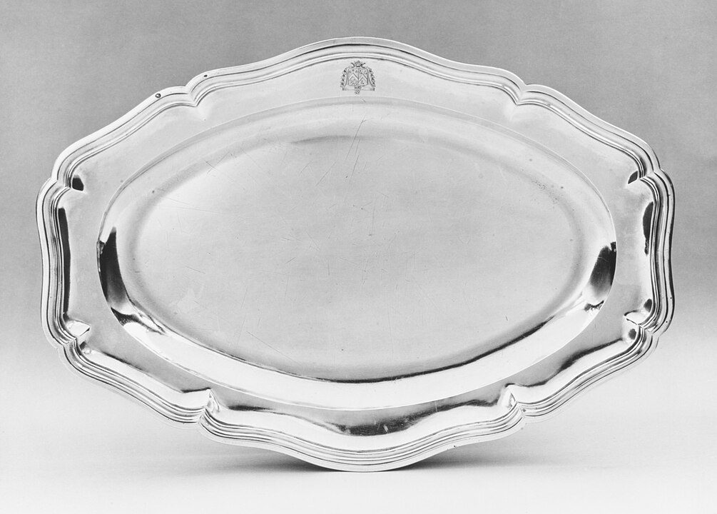 Silver serving tray, ornate edges, oval shape, polished reflective surface, displayed against plain background, vintage or classic design, elegant and formal appearance