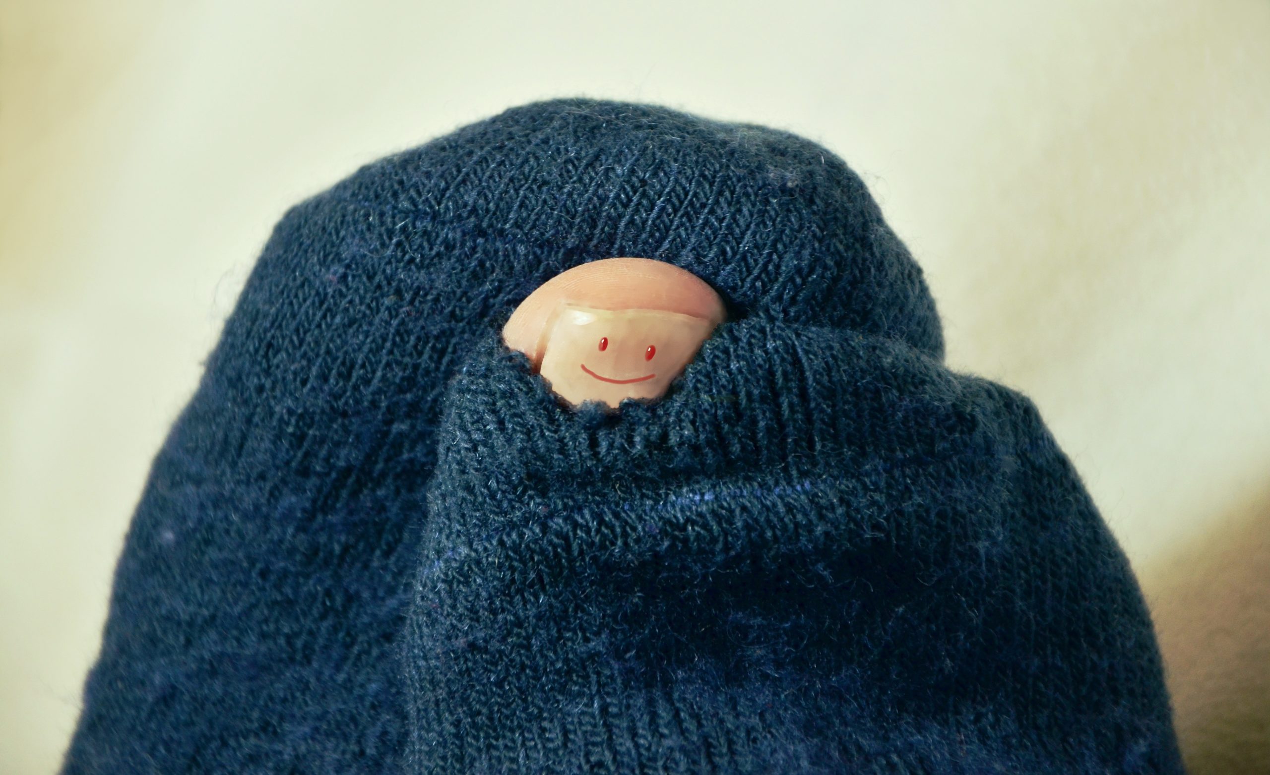 Toe with a smiley face drawn on the nail poking through a hole in a dark blue sock