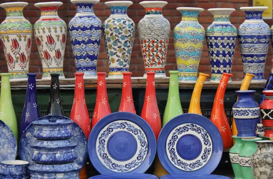 Colorful ceramic vases, plates, and bowls arranged on display at an outdoor market, with vibrant floral and geometric patterns against a brick wall backdrop