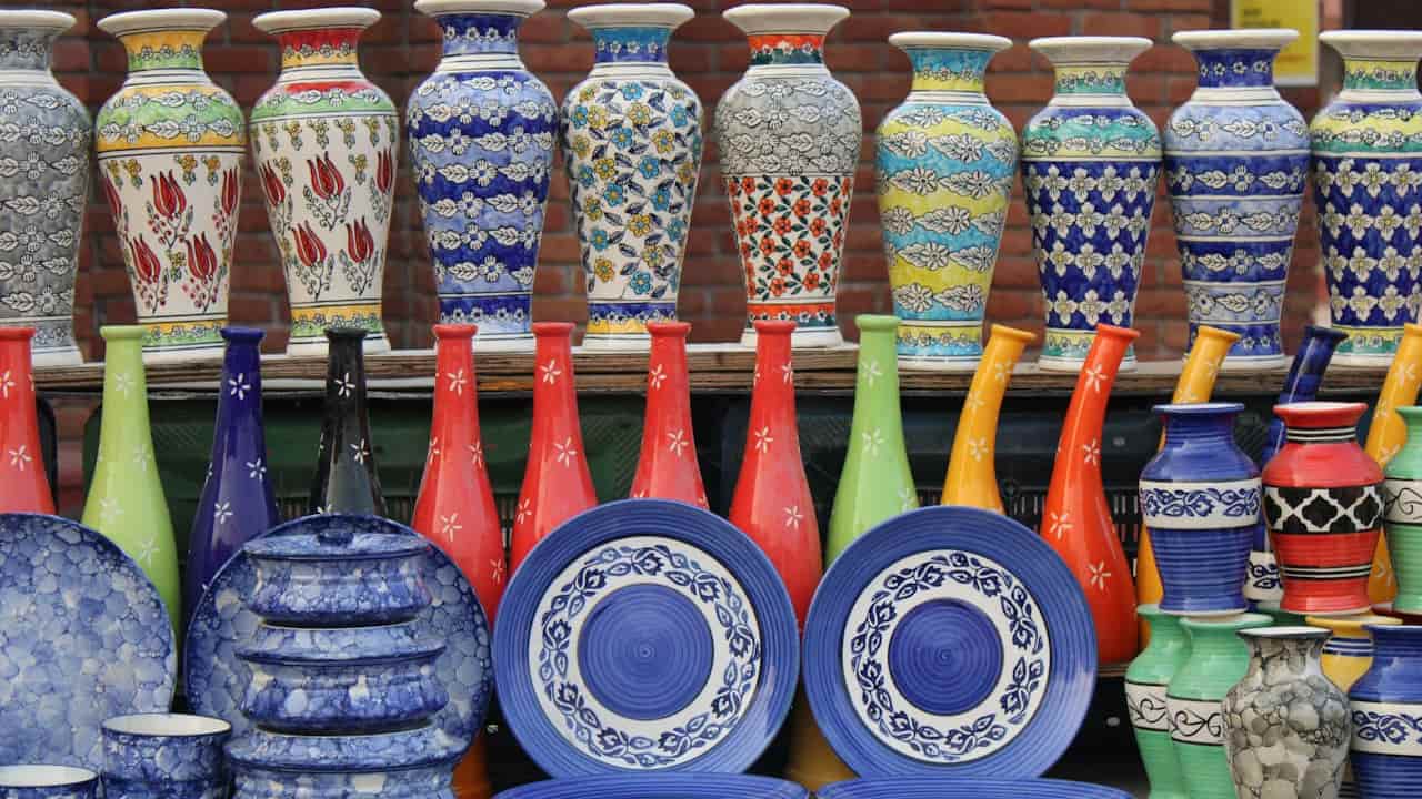 Colorful ceramic vases, plates, and bowls arranged on display at an outdoor market, with vibrant floral and geometric patterns against a brick wall backdrop