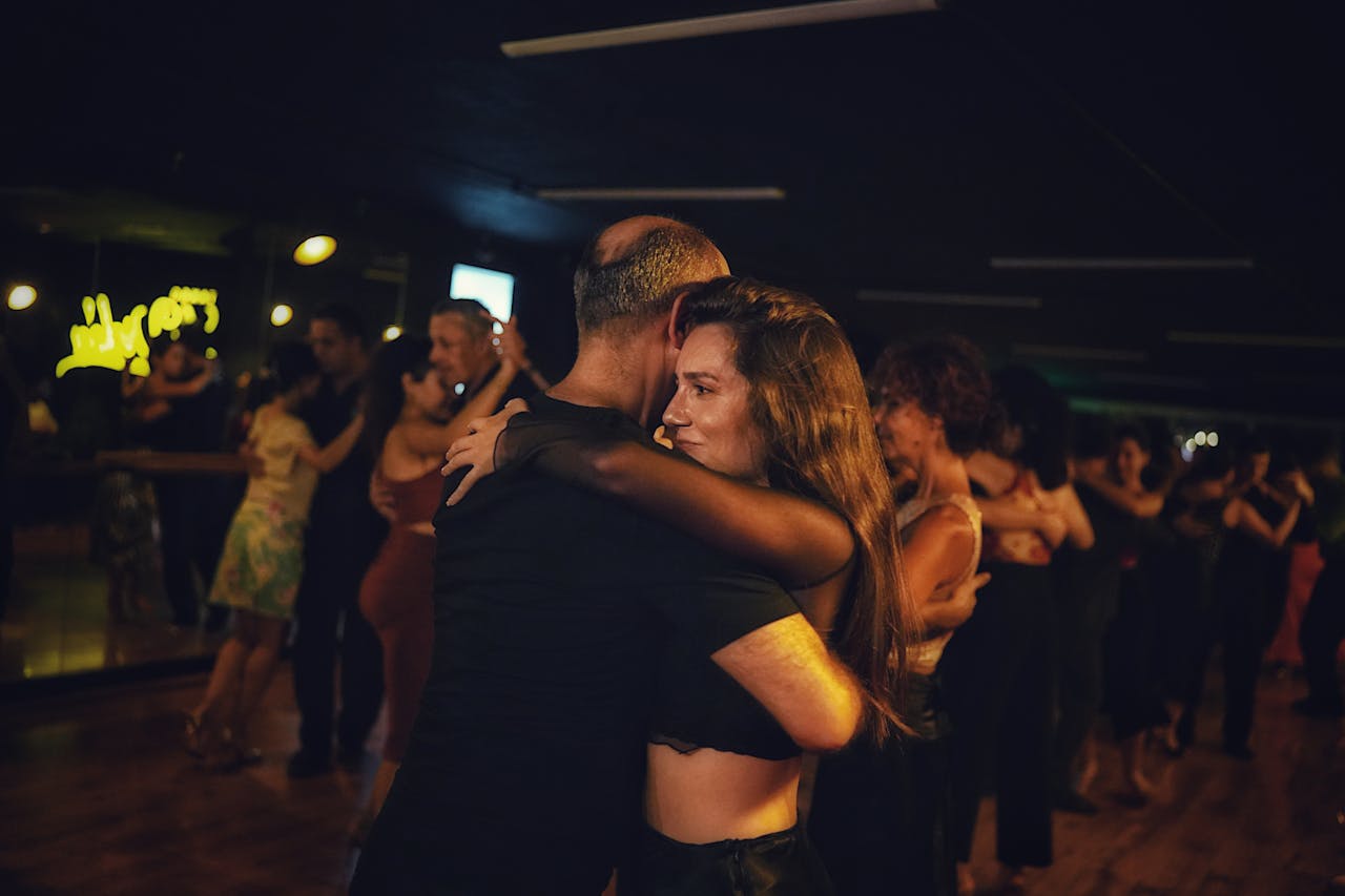 Couples dancing closely in a dimly lit room, wooden floor, intimate embrace, focus on one couple in the foreground