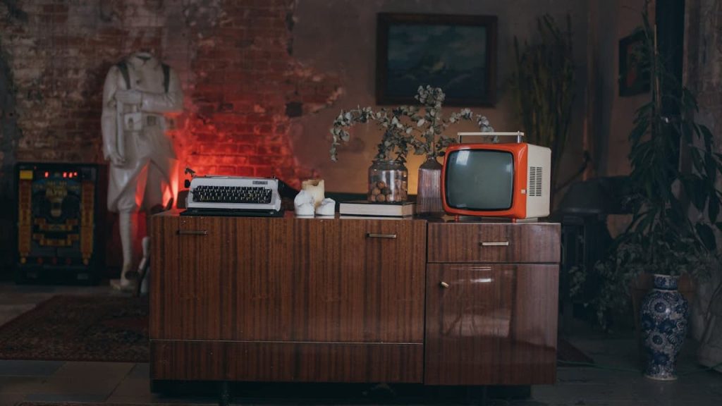 Vintage living room setup, wooden cabinet with retro television and radio, rotary phone, dried flowers in a vase, dim lighting with red glow on the left, worn walls