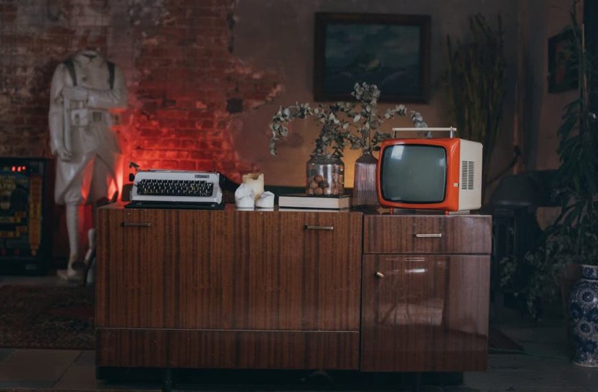 Vintage living room setup, wooden cabinet with retro television and radio, rotary phone, dried flowers in a vase, dim lighting with red glow on the left, worn walls