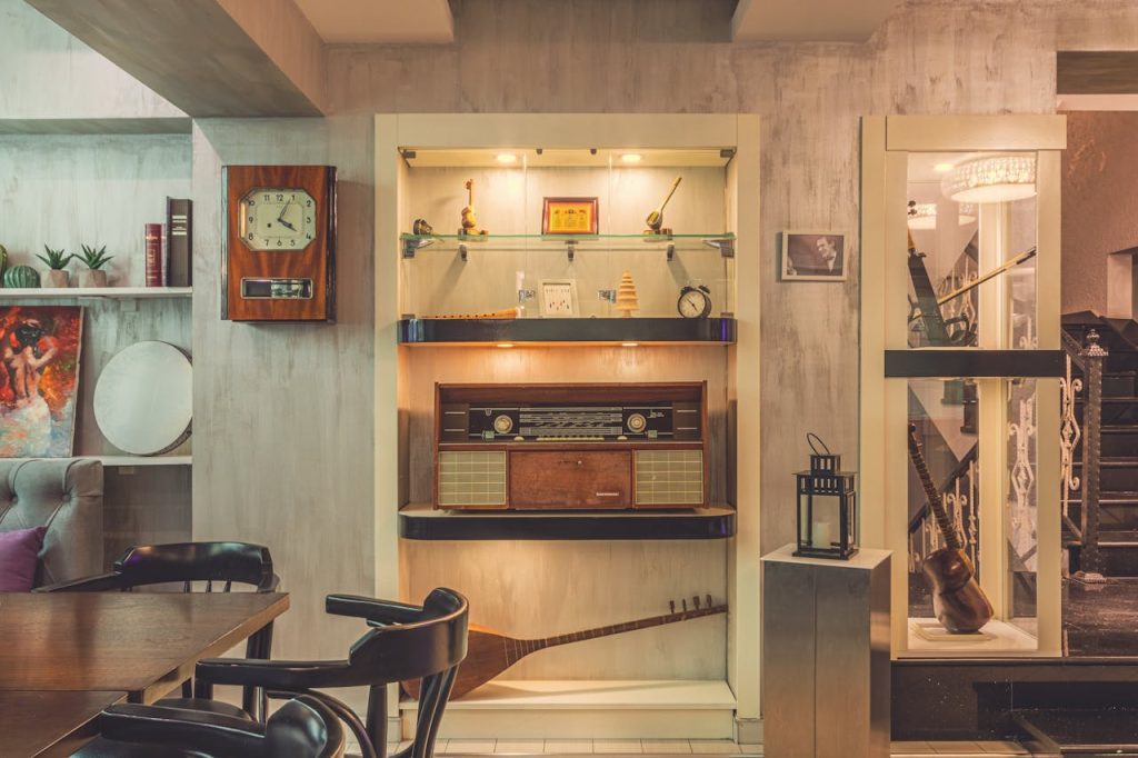 vintage-style interior room, wooden bar counter in the center, hanging glasses above the bar, antique clock on the wall, retro furnishings, display shelves with collectibles and glassware