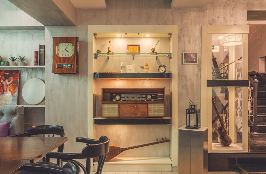 vintage-style interior room, wooden bar counter in the center, hanging glasses above the bar, antique clock on the wall, retro furnishings, display shelves with collectibles and glassware