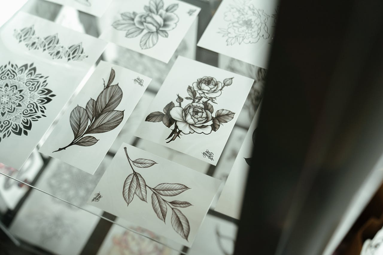 black and white floral and mandala tattoo designs laid out on white sheets displayed under glass