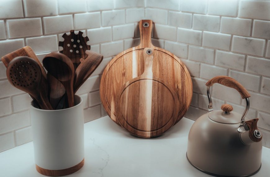Modern kitchen corner with wooden cooking utensils in a ceramic holder, two round wooden cutting boards, and a matte kettle with wooden accents