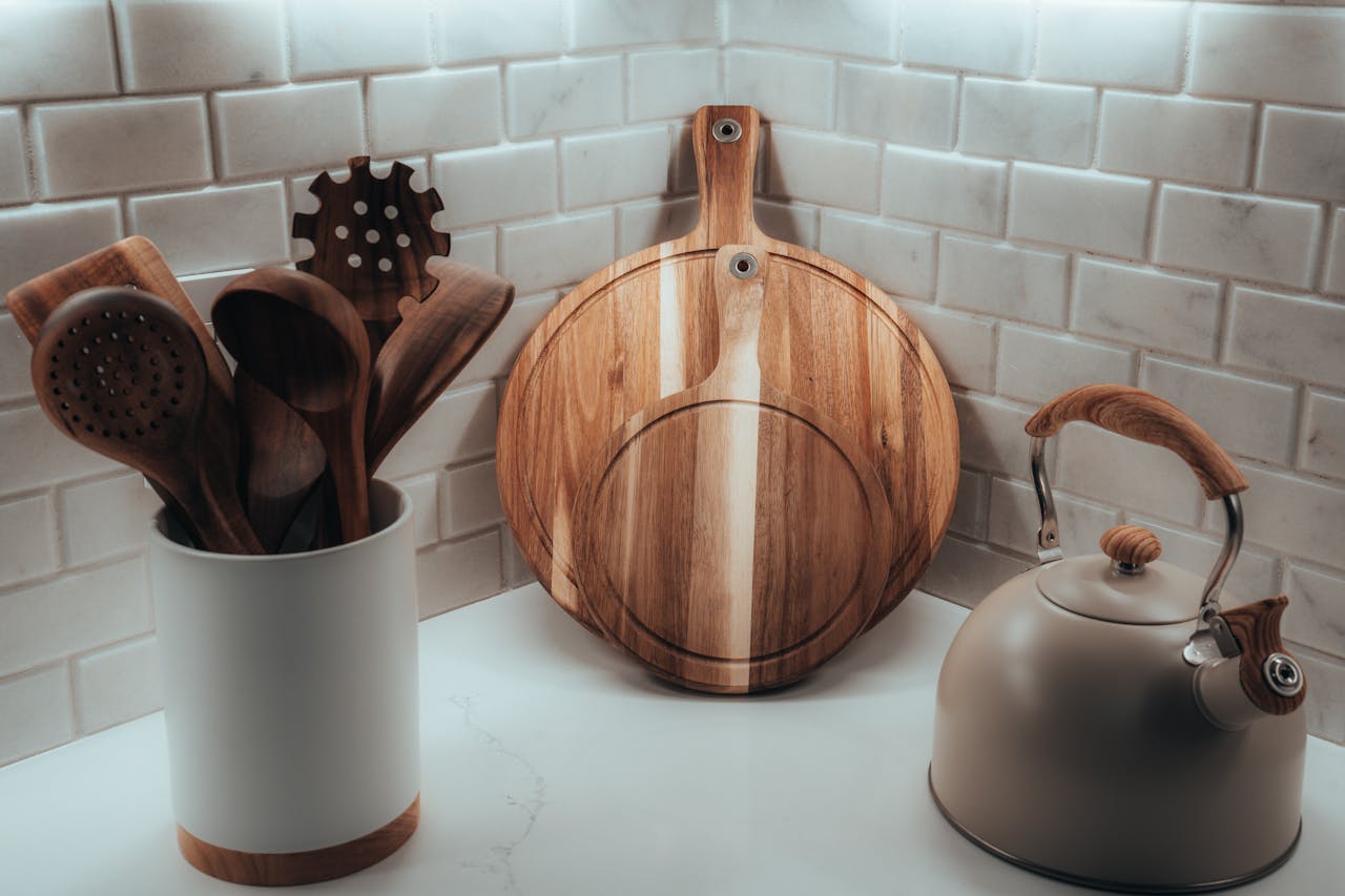 Modern kitchen corner with wooden cooking utensils in a ceramic holder, two round wooden cutting boards, and a matte kettle with wooden accents