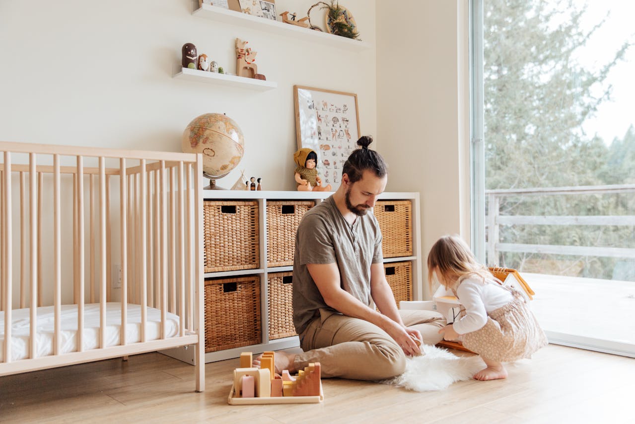 Father and daughter sitting on the floor, organizing toys together, wicker storage baskets in a shelf unit, wooden toy blocks on a tray, minimalistic nursery décor