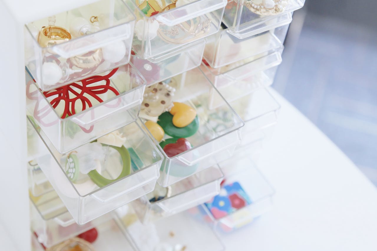 Clear plastic storage drawers containing various small items. Visible contents include colorful office supplies or craft materials. The transparent drawers are partially pulled out, showing organized storage of small objects in a stacked organizer unit