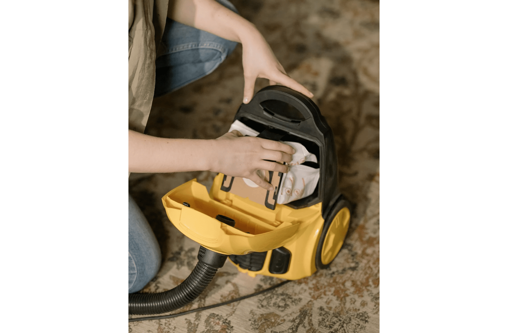 Person replacing a vacuum filter in a yellow canister vacuum on a patterned rug