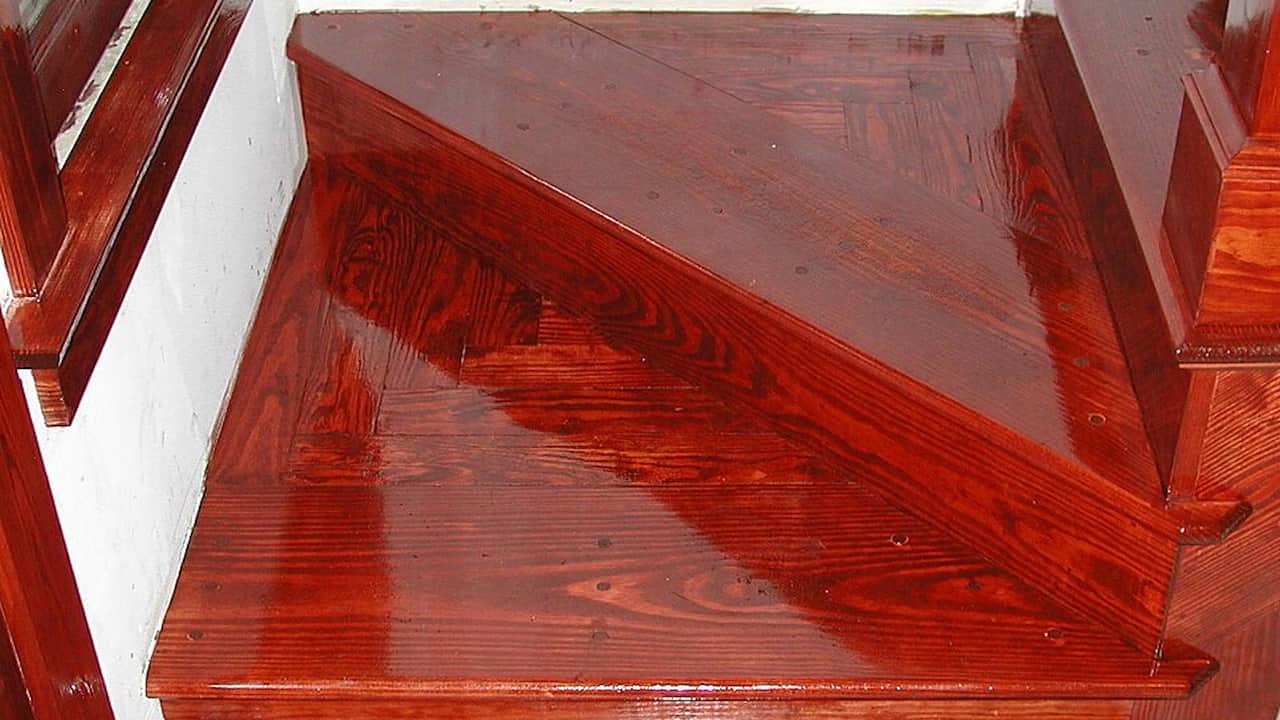 Glossy, varnished wooden staircase with rich reddish-brown finish and clear reflections indicating a freshly applied coat