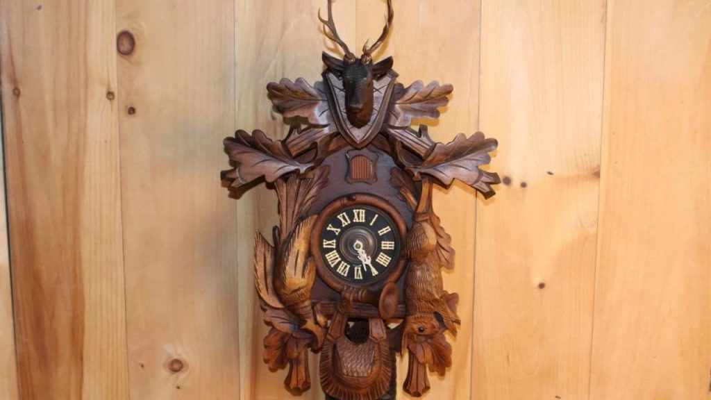 Ornately carved Black Forest cuckoo clock featuring a stag head with antlers, oak leaves, birds, and woodland animals, mounted on a wooden wall