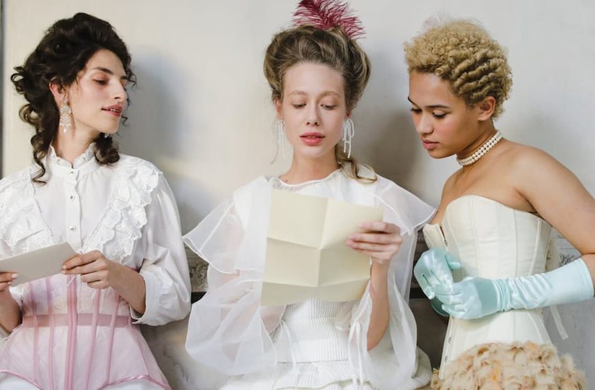Three women in vintage Victorian-inspired outfits, reading letters, wearing corsets, lace blouses, and pearl accessories, standing against a white wall