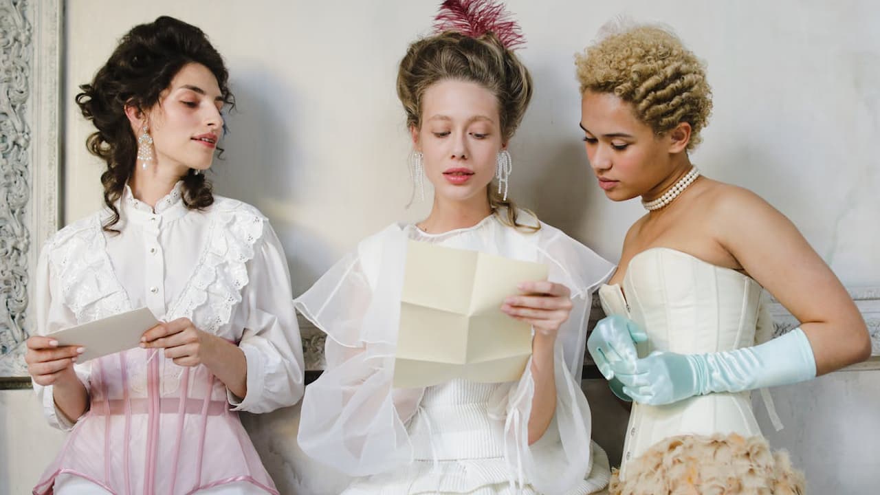 Three women in vintage Victorian-inspired outfits, reading letters, wearing corsets, lace blouses, and pearl accessories, standing against a white wall