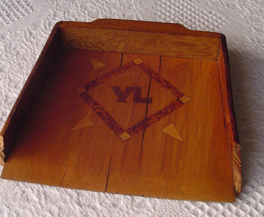 wooden tray, rectangular shape, raised edges, decorative design in the center with diamond pattern, letters "VL" inscribed, warm brown finish, placed on a textured white surface