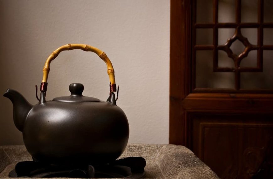 Black cast iron teapot, bamboo-wrapped handle, placed on a textured cloth, minimalistic background, wooden door with geometric glass panel, soft ambient lighting