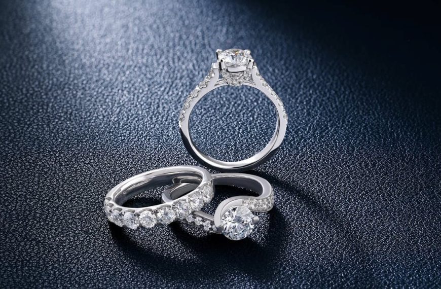 Three elegant diamond rings, silver bands with various stone settings, placed on a dark textured surface, spotlight highlighting their sparkle and clarity