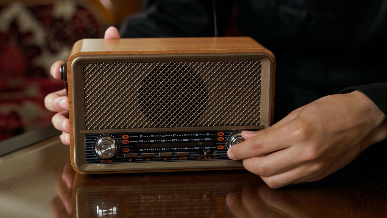 person adjusting vintage sound system, wood-paneled stereo, large analog knobs, vinyl record player on top, classic speaker setup, retro audio equipment