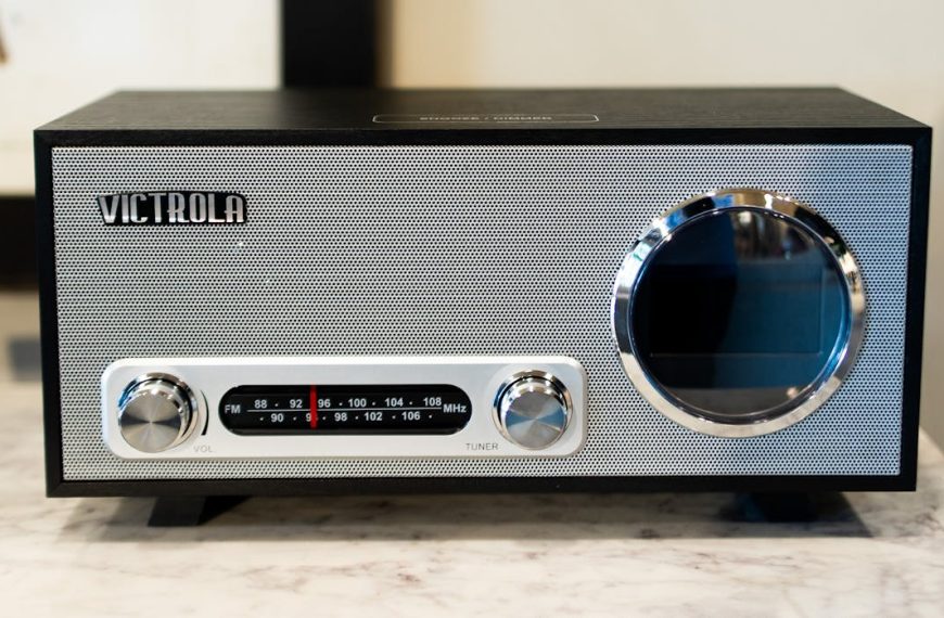 Black and silver Victrola retro radio, front-facing view, two control knobs labeled volume and tuner, FM/AM frequency display in the center, circular speaker on the right, placed on a marble surface indoors