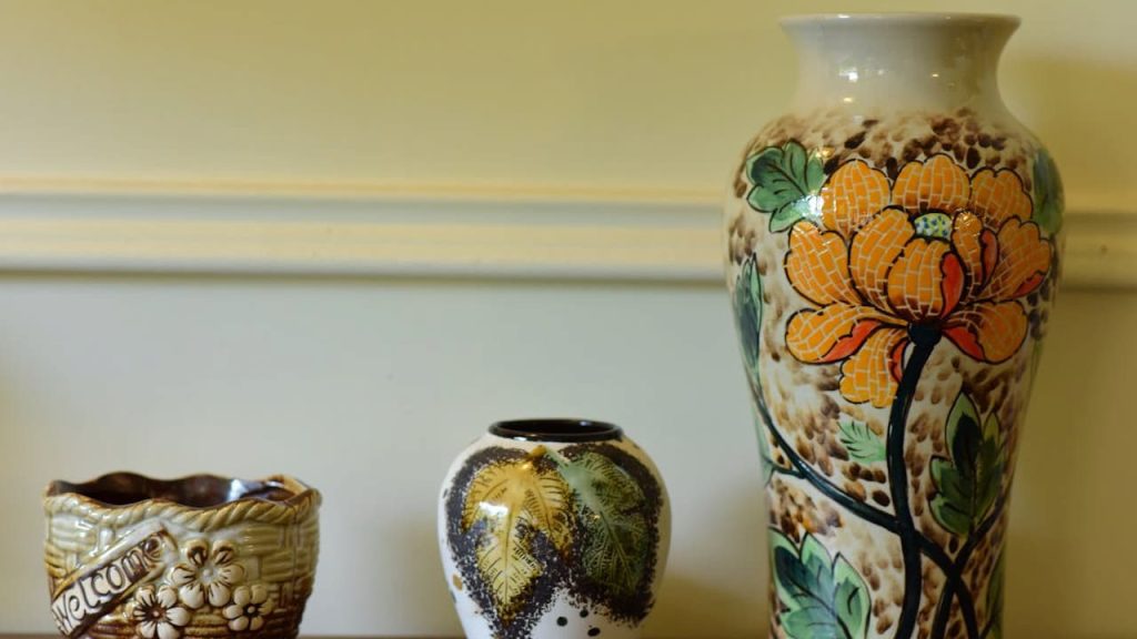 Three decorative ceramic vases, placed on a shelf, varying sizes and shapes, intricate floral and nature-themed patterns, warm earthy tones, light yellow wall background