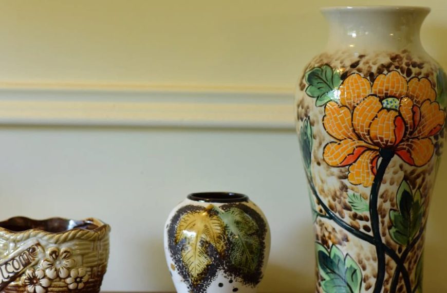 Three decorative ceramic vases, placed on a shelf, varying sizes and shapes, intricate floral and nature-themed patterns, warm earthy tones, light yellow wall background