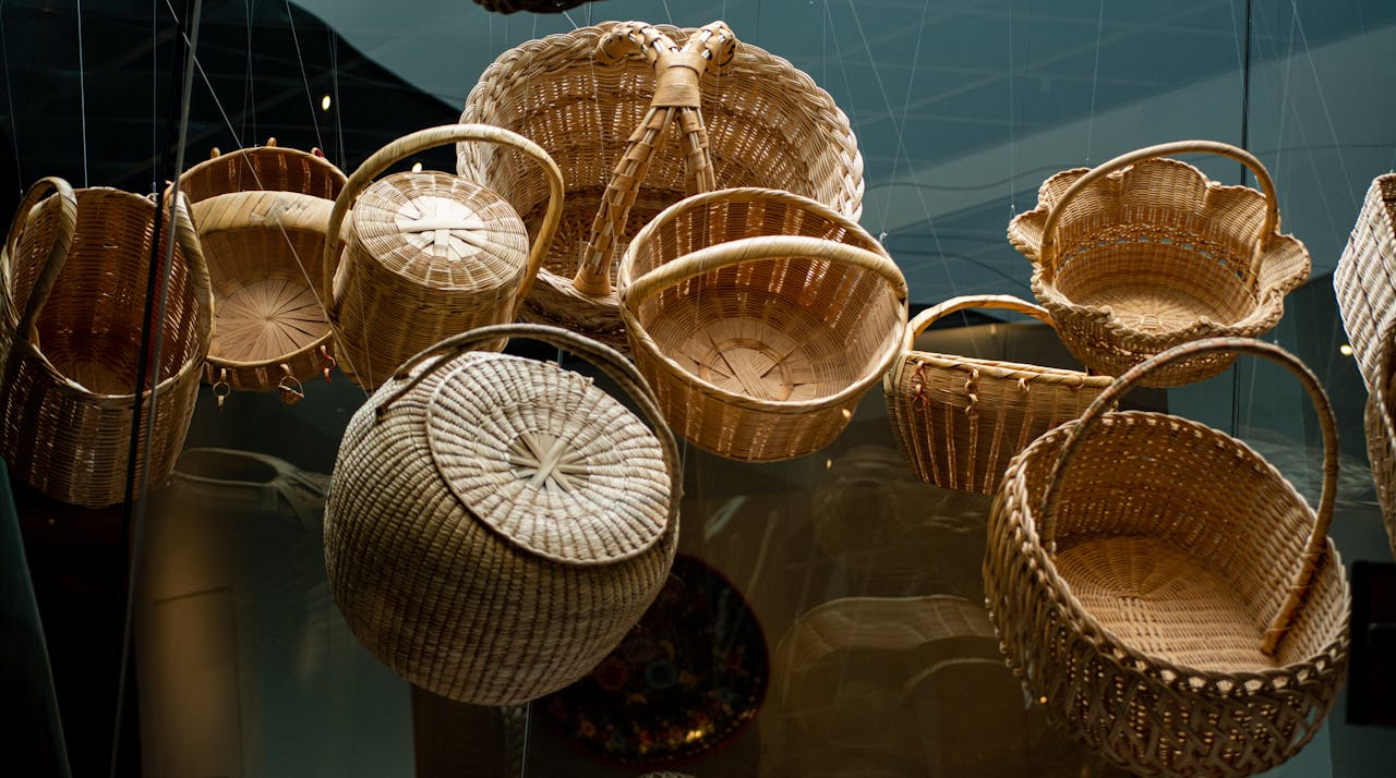 Collection of intricately woven baskets in various shapes and sizes, displayed on a reflective surface, made from natural materials