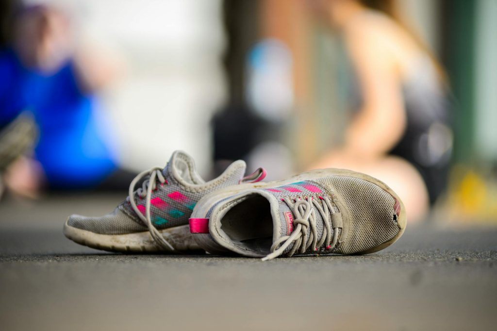 Worn out shoes, scuffed soles, faded fabric, frayed laces, creased leather or canvas, visible dirt and wear, placed on rough surface or floor