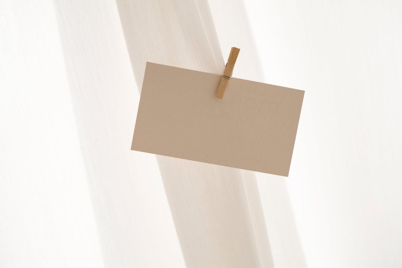 Neutral-colored card clipped with a wooden clothespin, hanging against a soft, white fabric backdrop, creating a minimalist and airy aesthetic