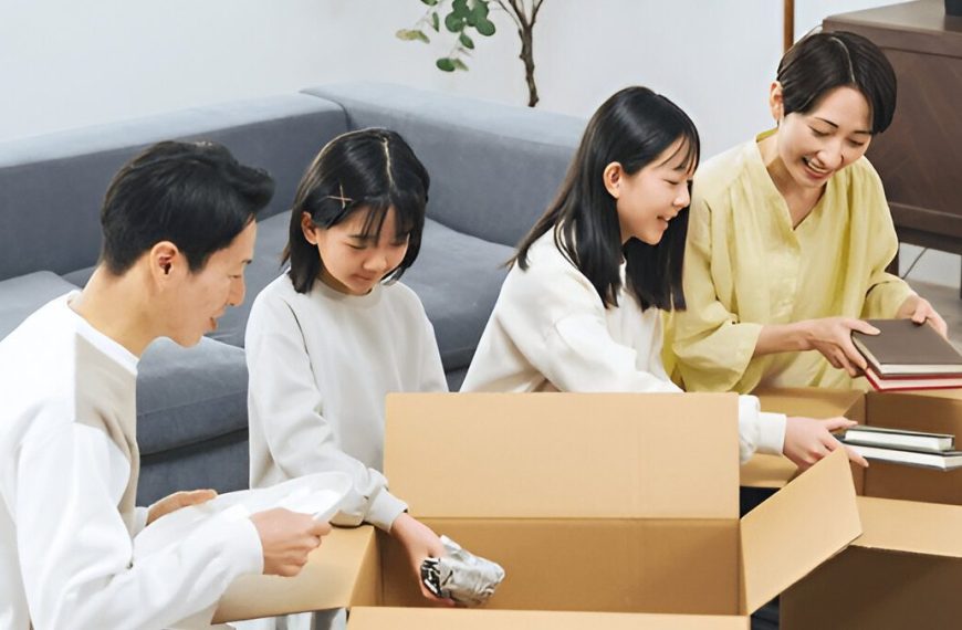 A smiling family of four sitting in a living room, unpacking items from cardboard boxes together