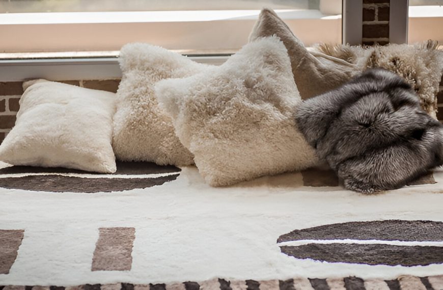 Plush decorative pillows on a cozy bed, soft beige and cream tones, various textures including faux fur, patterned blanket underneath, warm and inviting atmosphere, natural light softly illuminating the scene