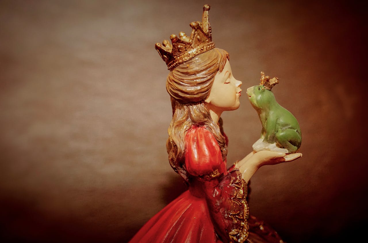 Princess figurine in red gown with golden crown holding and kissing a green frog wearing a small crown