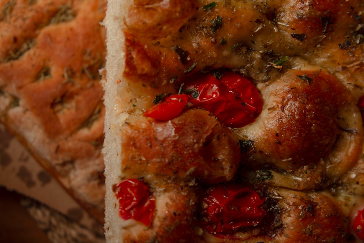 Close-up of freshly baked focaccia topped with roasted red cherry tomatoes, herbs, and a golden, crispy crust