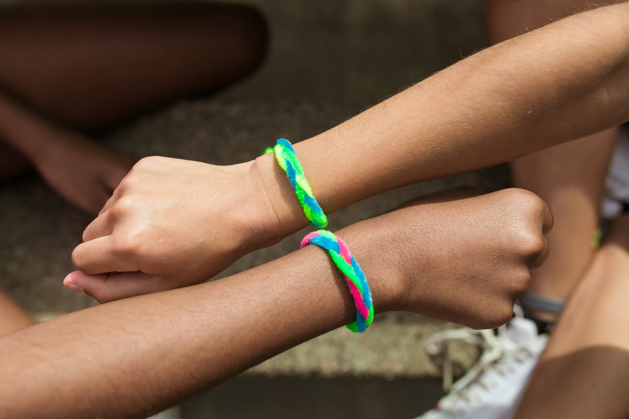 Two arms wearing colorful braided friendship bracelets, touching fists in a gesture of unity