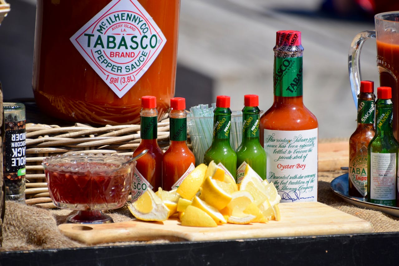 Assortment of Tabasco hot sauce bottles in various sizes and flavors, alongside sliced lemons, a bowl of cocktail sauce