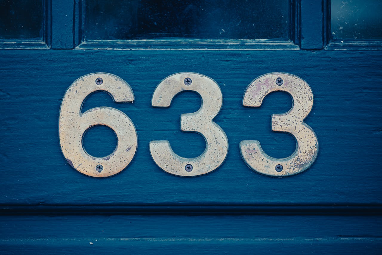 Close-up of metal house numbers “633” mounted on a dark blue wooden door