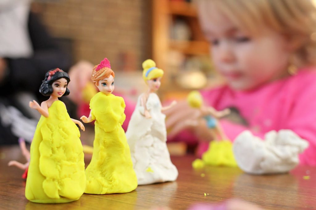 Young child crafting colorful clay dresses on small princess dolls during a creative indoor play session