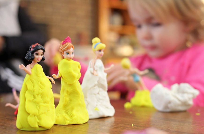 Young child crafting colorful clay dresses on small princess dolls during a creative indoor play session