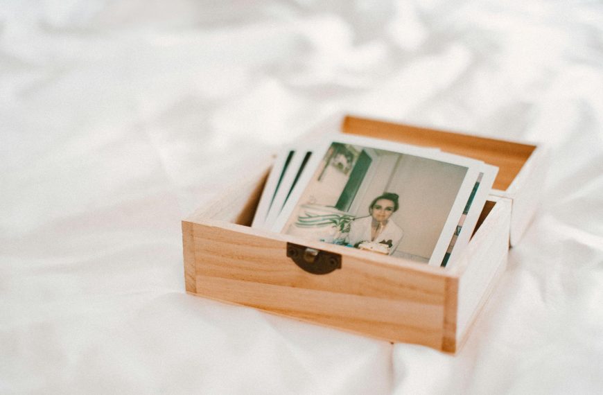 Wooden box filled with printed Polaroid photos, placed on a white fabric surface, nostalgic memory collection, keepsake storage